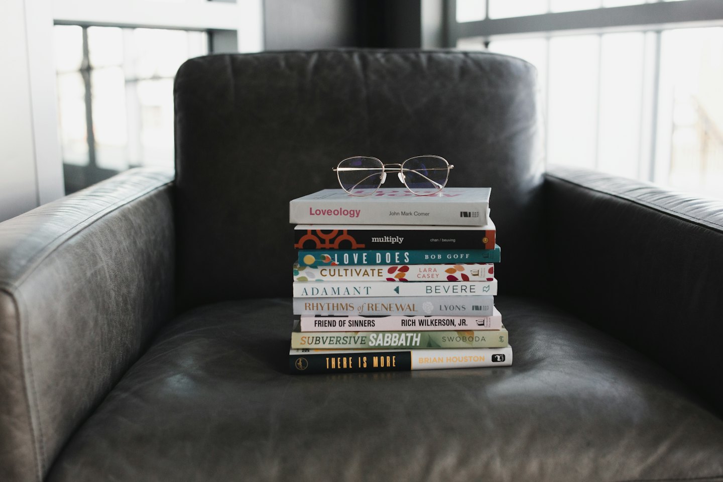 Gold-rimmed reading glasses on a stack of books on a leather armchair.