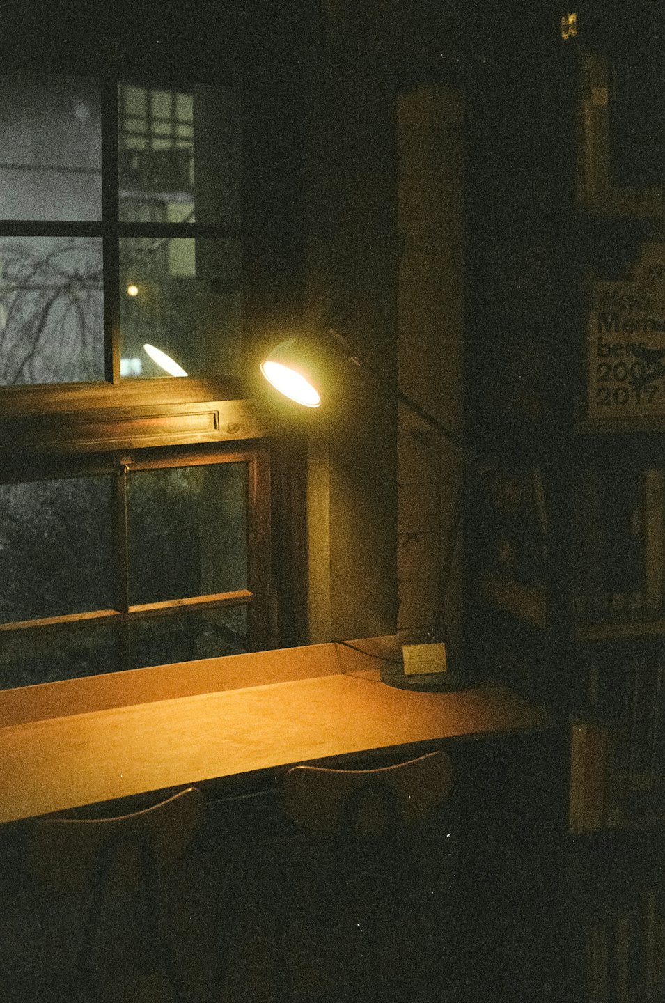 An empty wooden desk sits by a window at night.