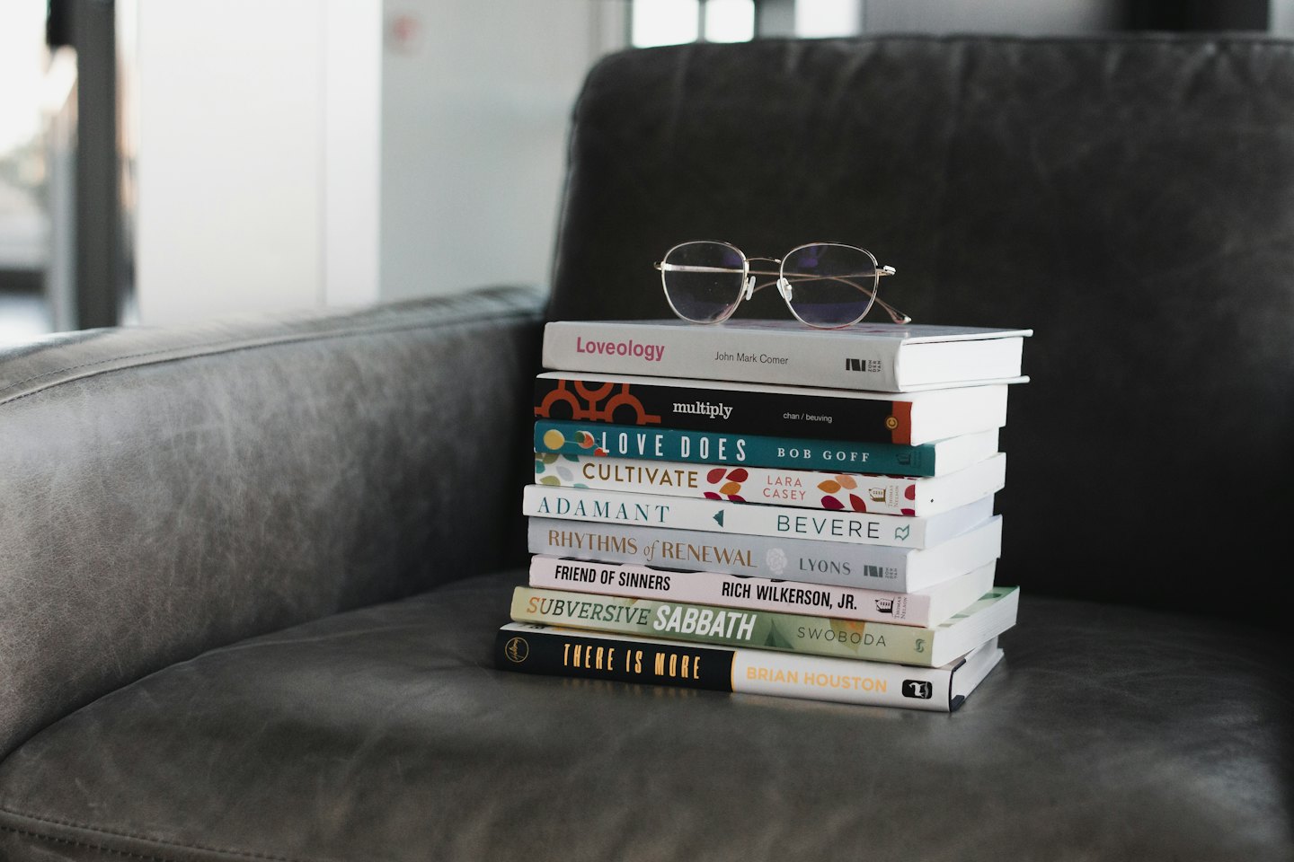 Books and reading glasses on a grey leather armchair.